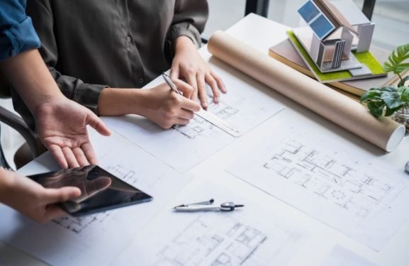 Architect reviewing floor plans and building blueprints on a workspace desk.